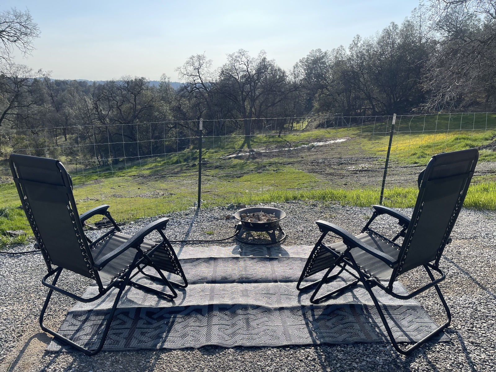 Two outdoor lounge chairs facing a field at the farm in Placerville, California, with a fire pit and oak-dotted hills